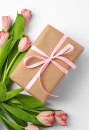 Photo of Beautiful gift box with bow and pink tulips on white background, flat lay