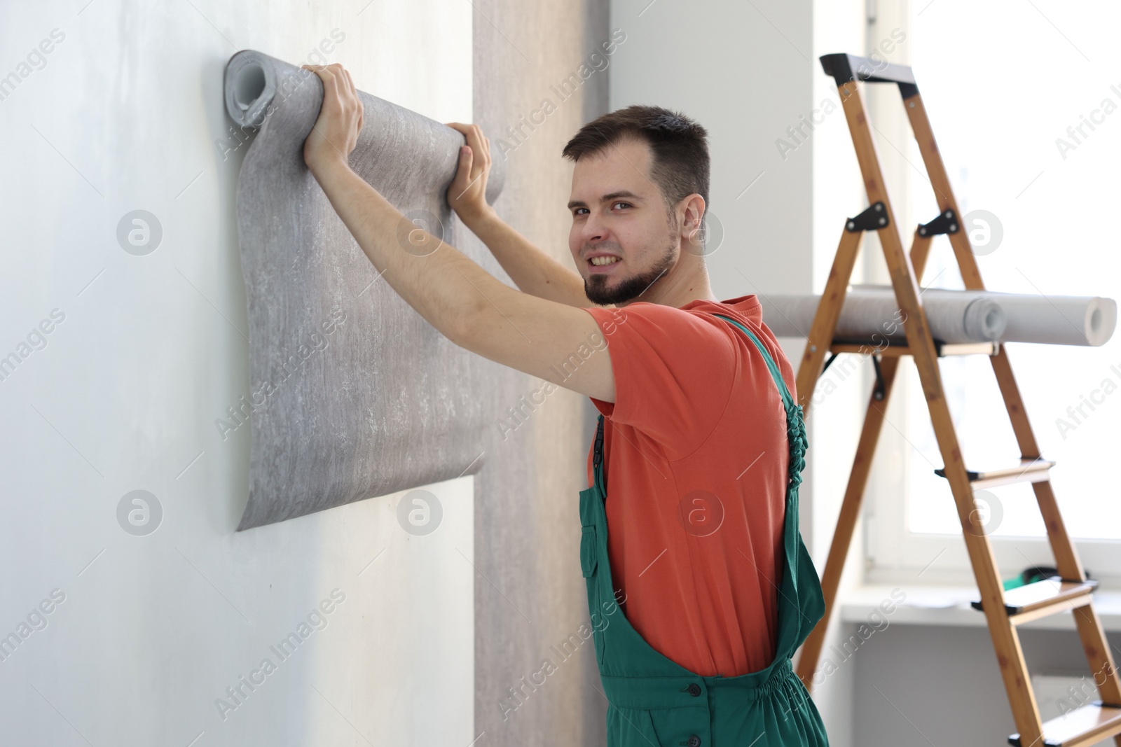 Photo of Man hanging stylish gray wallpaper in room