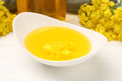Photo of Rapeseed oil in gravy boat and beautiful yellow flowers on white wooden table, closeup
