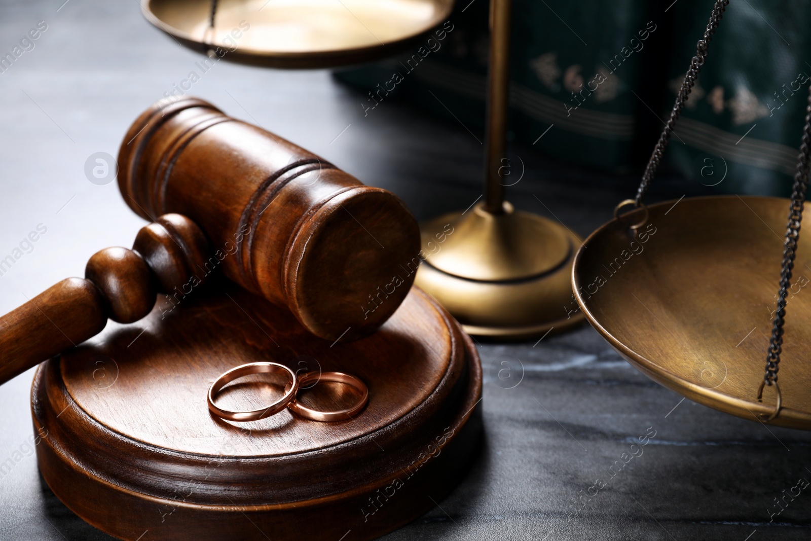 Photo of Divorce concept. Wooden gavel with wedding rings on black table, closeup