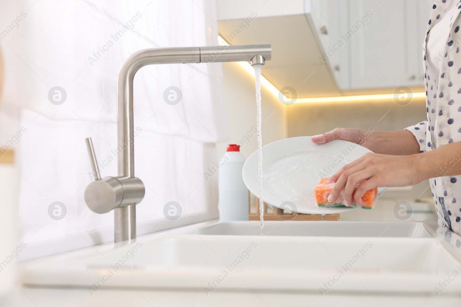 Photo of Woman washing plate above sink in modern kitchen, closeup