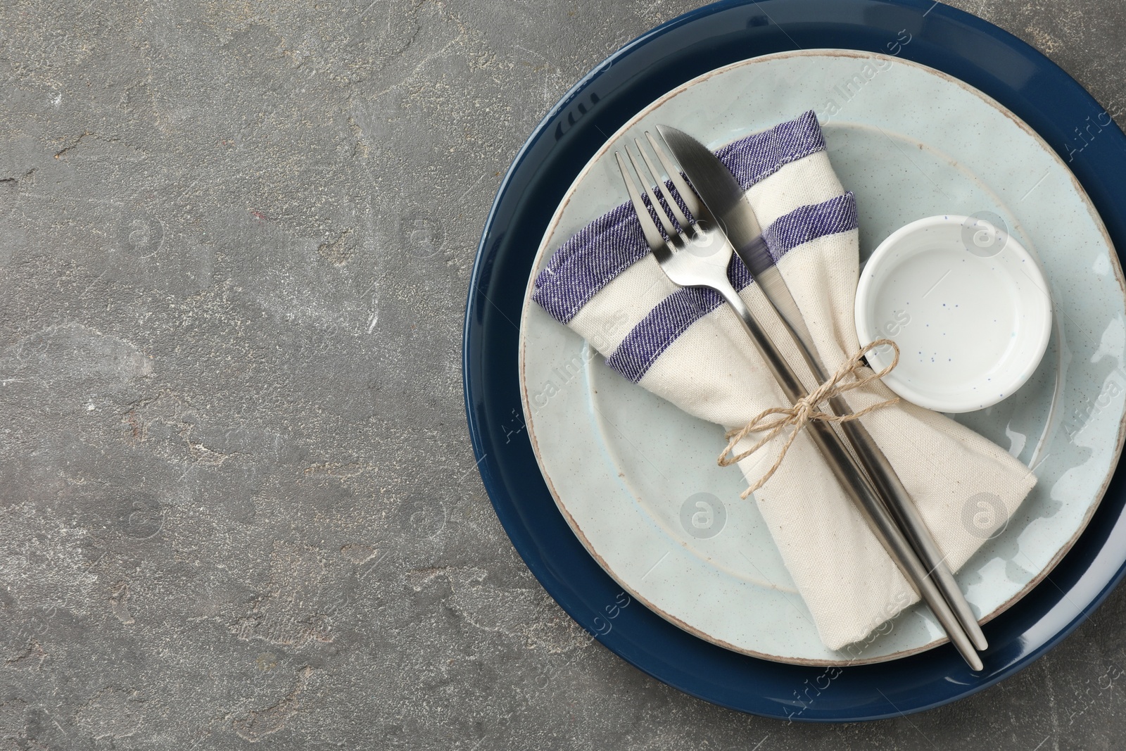 Photo of Stylish setting with cutlery, plates, bowl and napkin on grey textured table, top view. Space for text