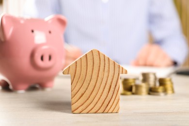 Woman planning budget at table, focus on wooden house model