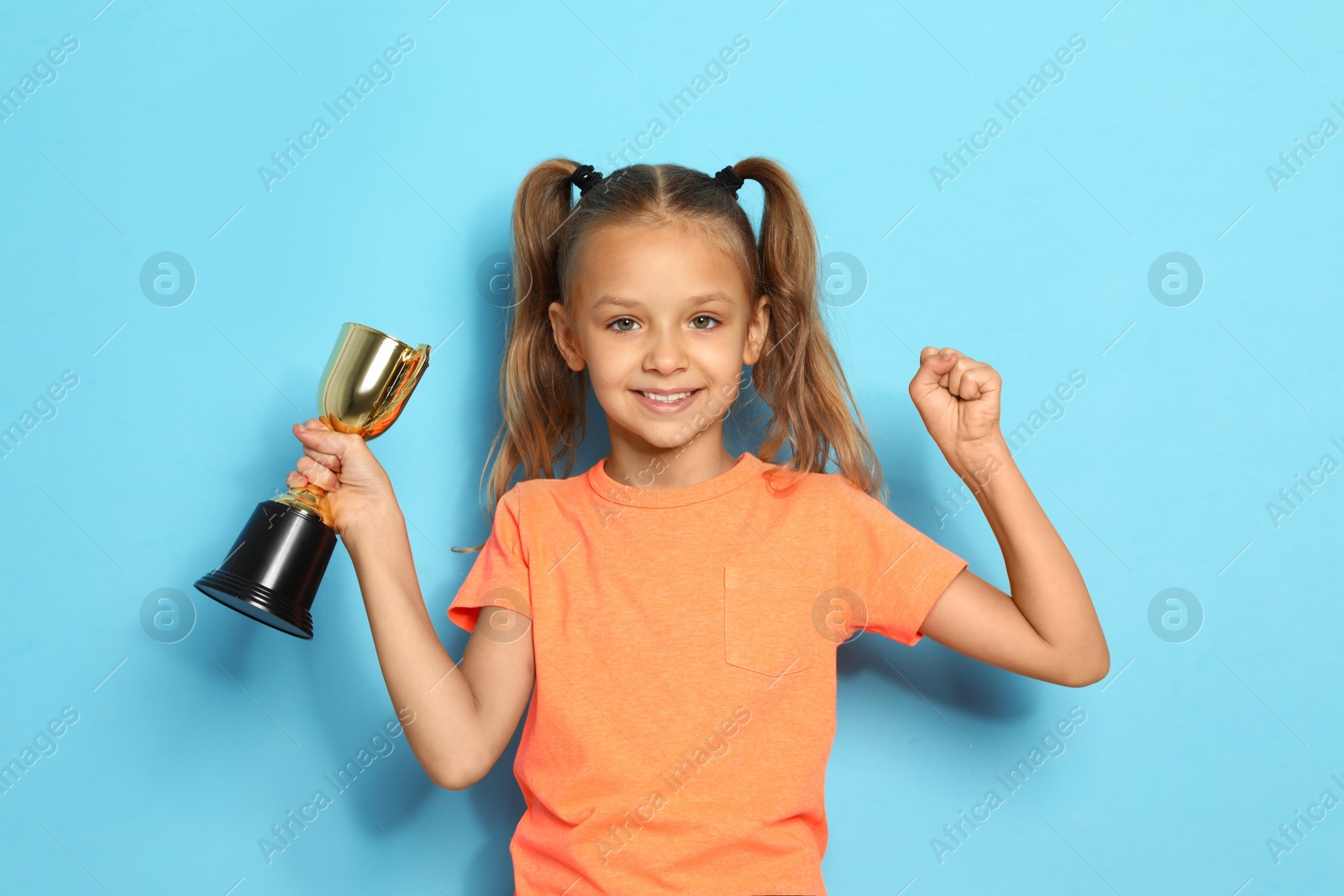 Photo of Happy girl with golden winning cup on blue background