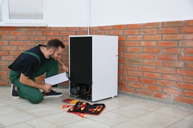 Male technician with clipboard examining refrigerator indoors. Space for text