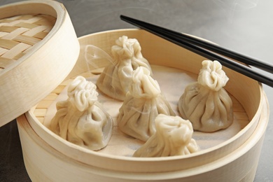 Photo of Bamboo steamer with tasty baozi dumplings and chopsticks on table, closeup