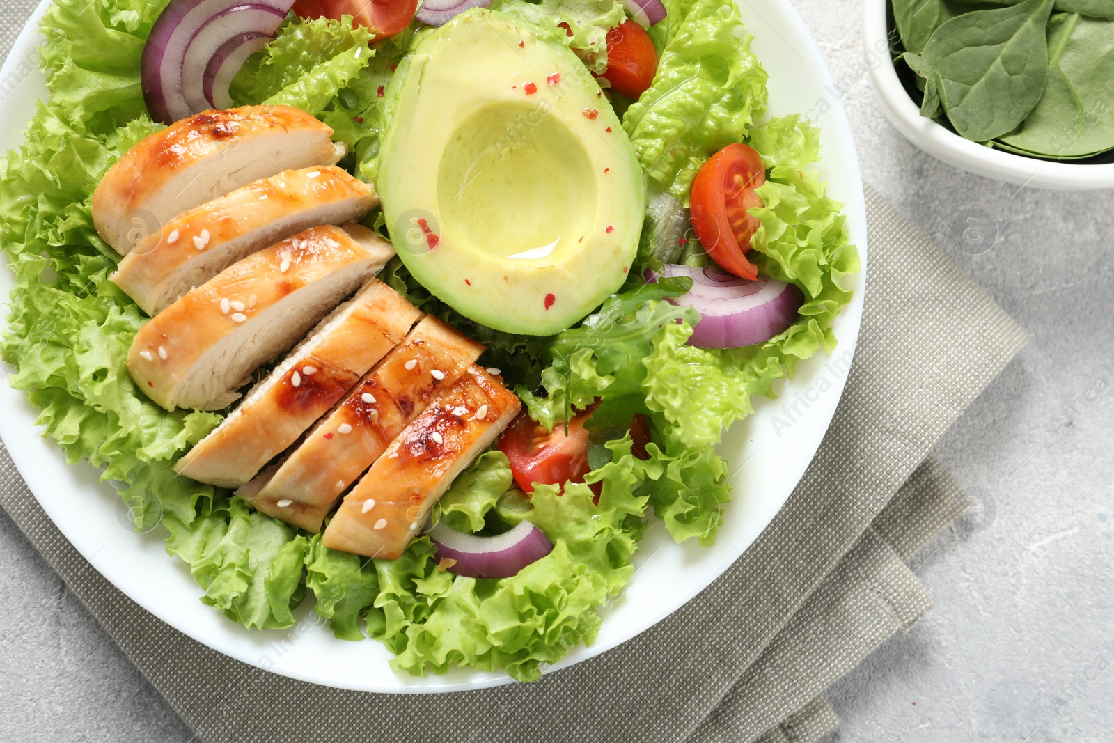 Photo of Delicious salad with chicken, avocado and vegetables on light grey table, top view