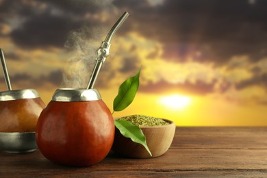 Image of Calabashes with mate tea and bombilla on wooden table outdoors at sunset. Space for text