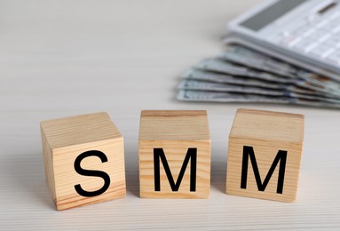 Cubes with abbreviation SMM (Social media marketing), money and calculator on white wooden table