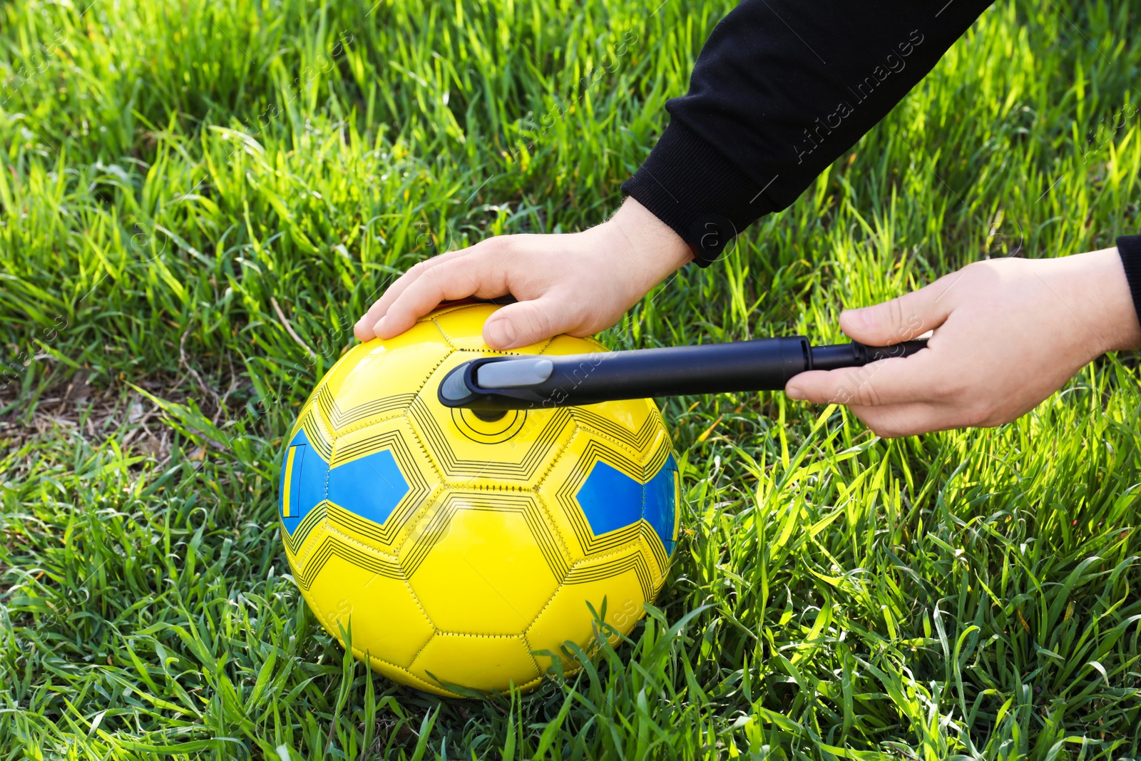 Photo of Man inflating soccer ball with manual pump on green grass, closeup