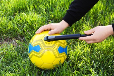 Photo of Man inflating soccer ball with manual pump on green grass, closeup