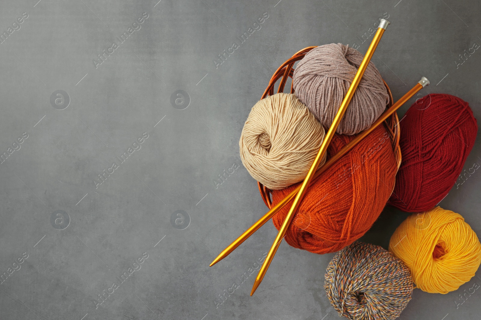 Photo of Different balls of woolen knitting yarns and needles on grey background, flat lay. Space for text