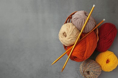 Photo of Different balls of woolen knitting yarns and needles on grey background, flat lay. Space for text