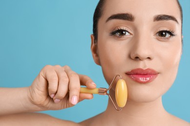 Photo of Woman using natural jade face roller on light blue background, closeup