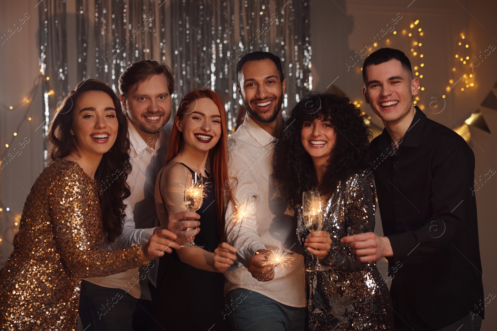 Photo of Happy friends with glasses of wine and sparklers celebrating birthday indoors