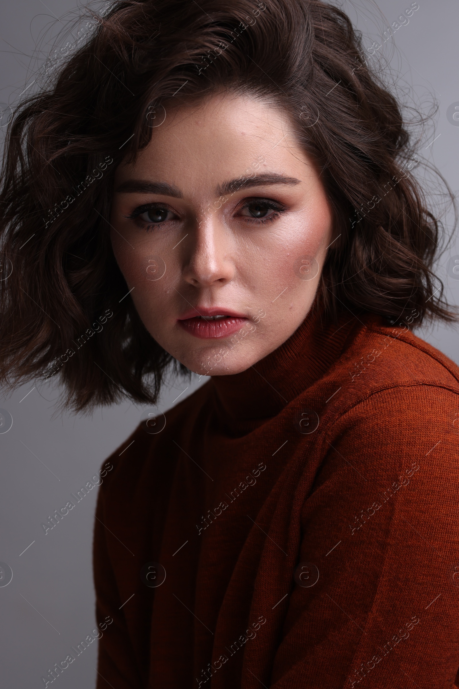 Photo of Portrait of beautiful young woman with wavy hairstyle on grey background