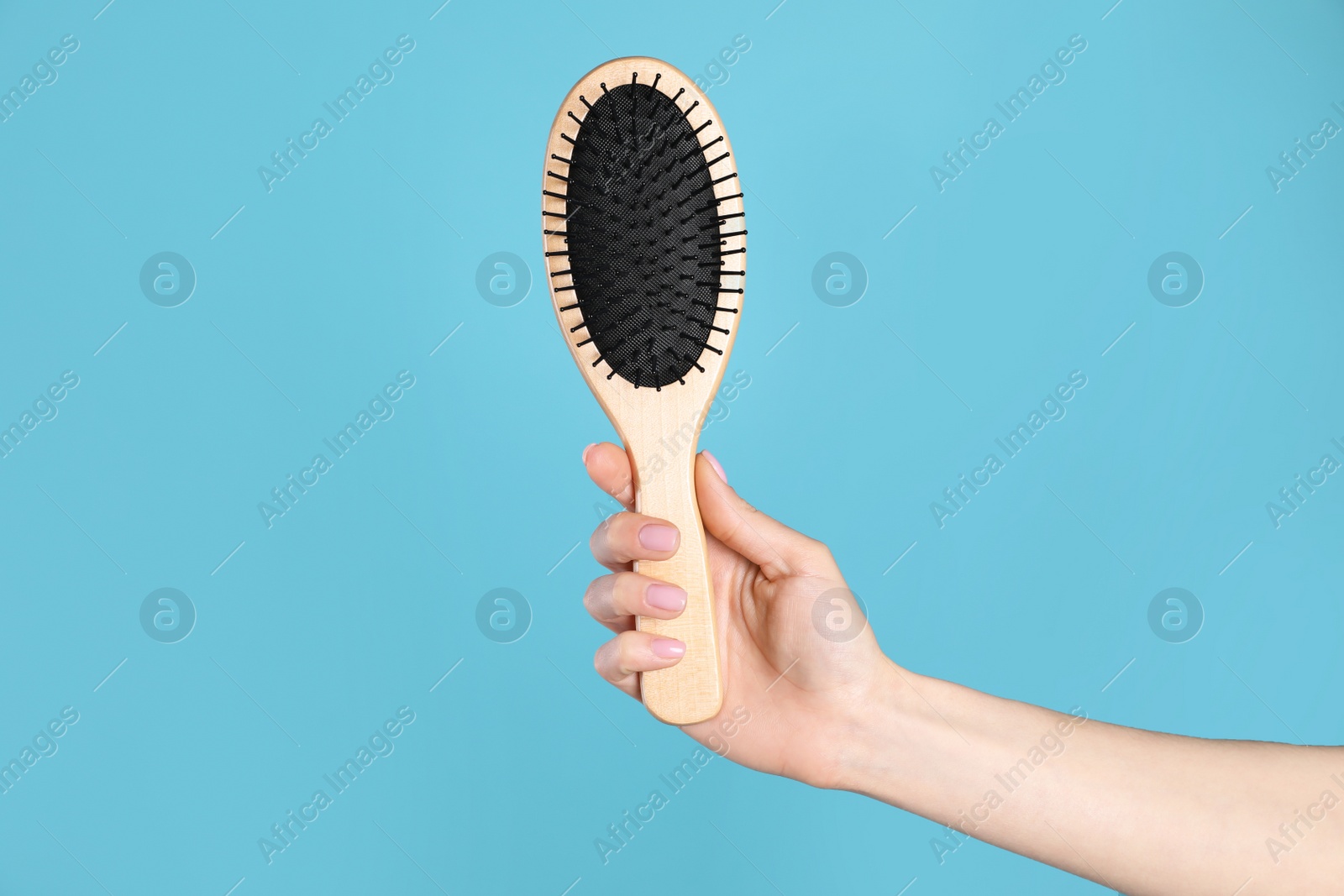 Photo of Woman holding wooden hair brush against blue background, closeup. Space for text