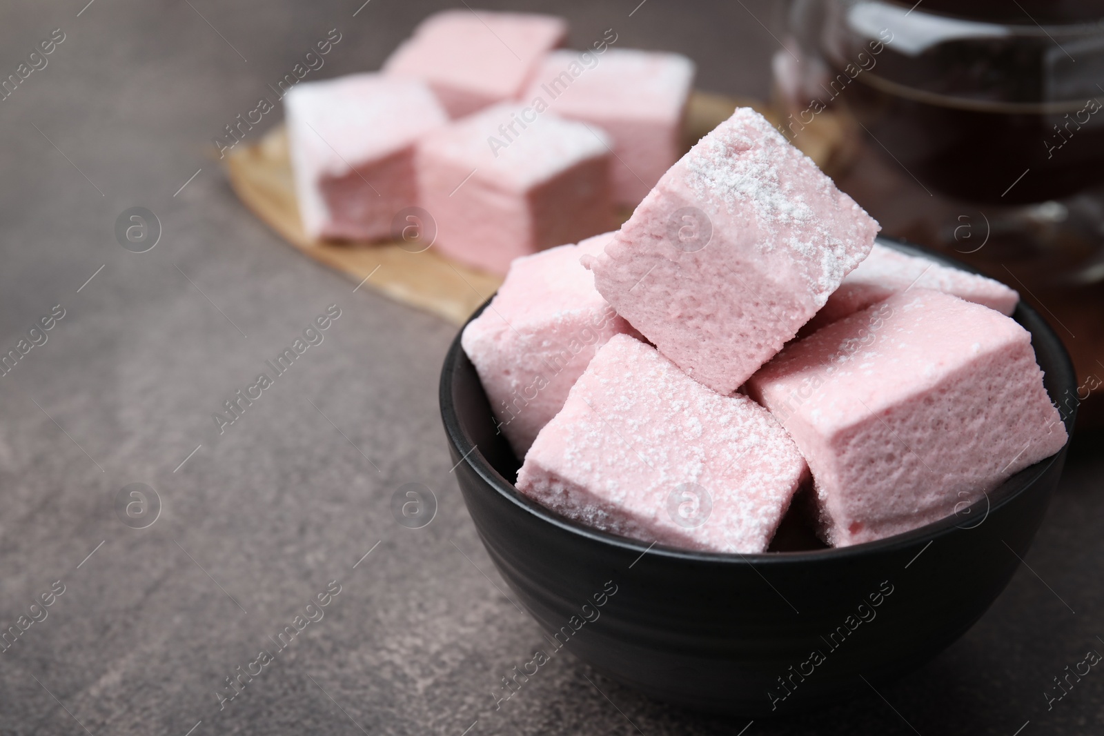 Photo of Bowl of delicious sweet marshmallows with powdered sugar on brown table, closeup. Space for text