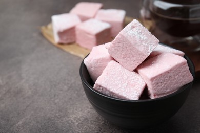 Bowl of delicious sweet marshmallows with powdered sugar on brown table, closeup. Space for text