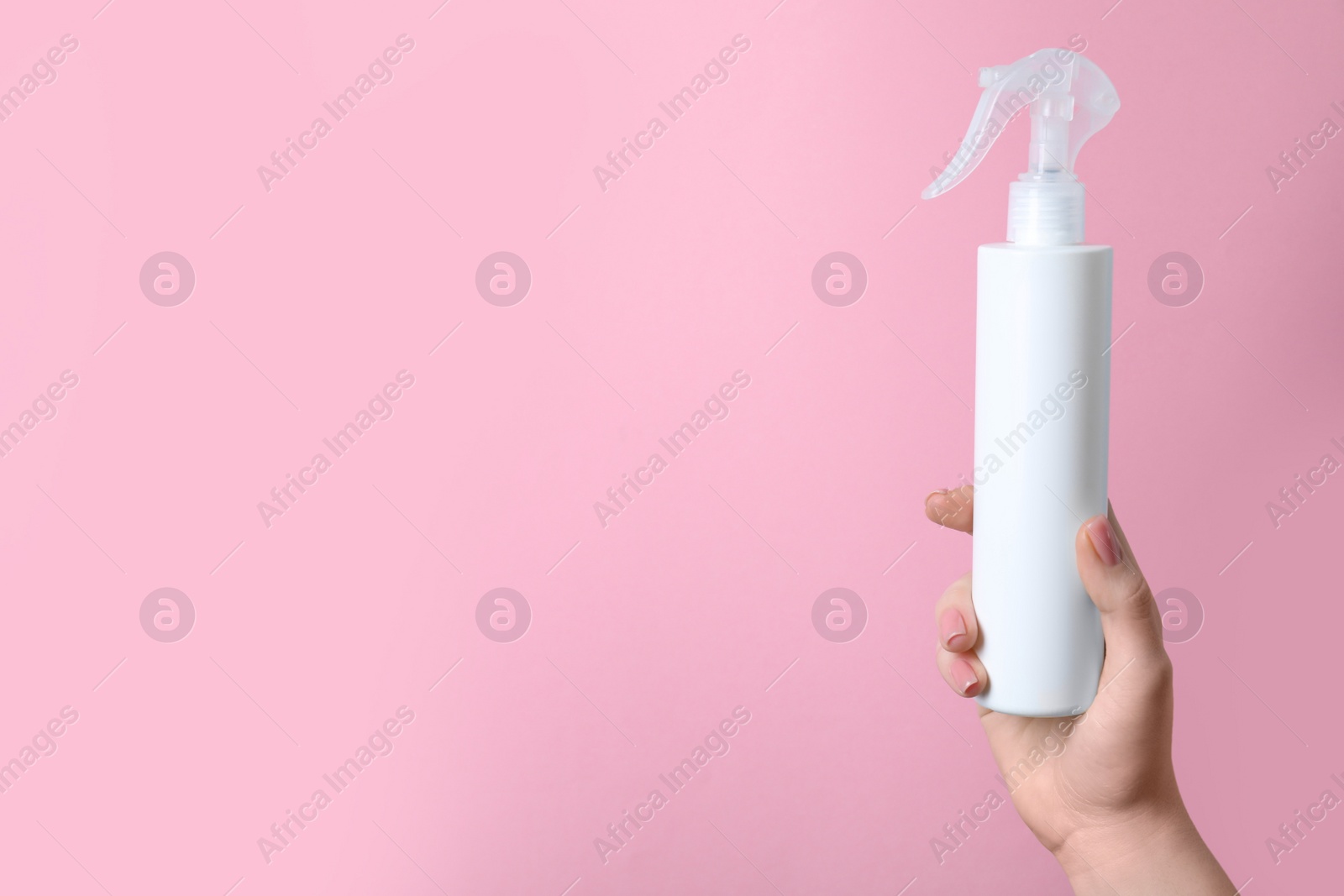 Photo of Woman holding spray bottle with thermal protection on light pink background, closeup. Space for text