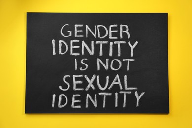 Photo of Blackboard with text Gender Identity Is Not Sexual Identity on yellow background, top view
