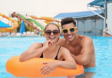 Happy couple with inflatable ring in swimming pool at water park