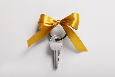 Photo of Key with yellow bow on light grey background, top view. Housewarming party