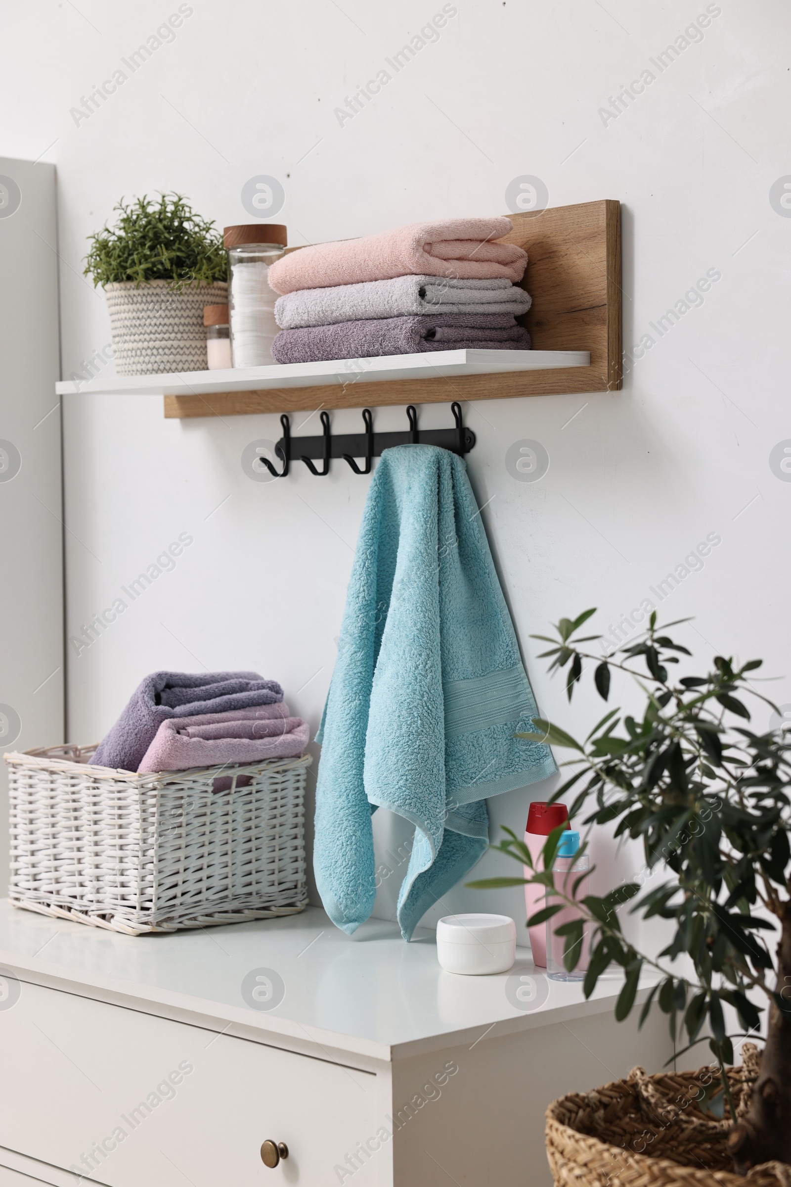Photo of Fresh towels, laundry basket and toiletries on chest of drawers indoors