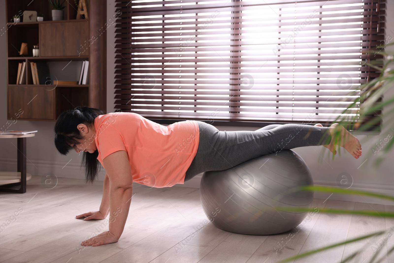 Photo of Overweight mature woman doing exercise with fitness ball at home