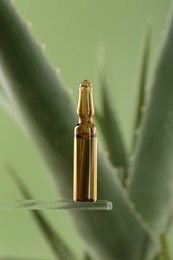 Skincare ampoule near aloe vera on light green background, closeup