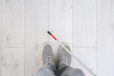 Photo of Blind person with long cane standing indoors, top view. Space for text