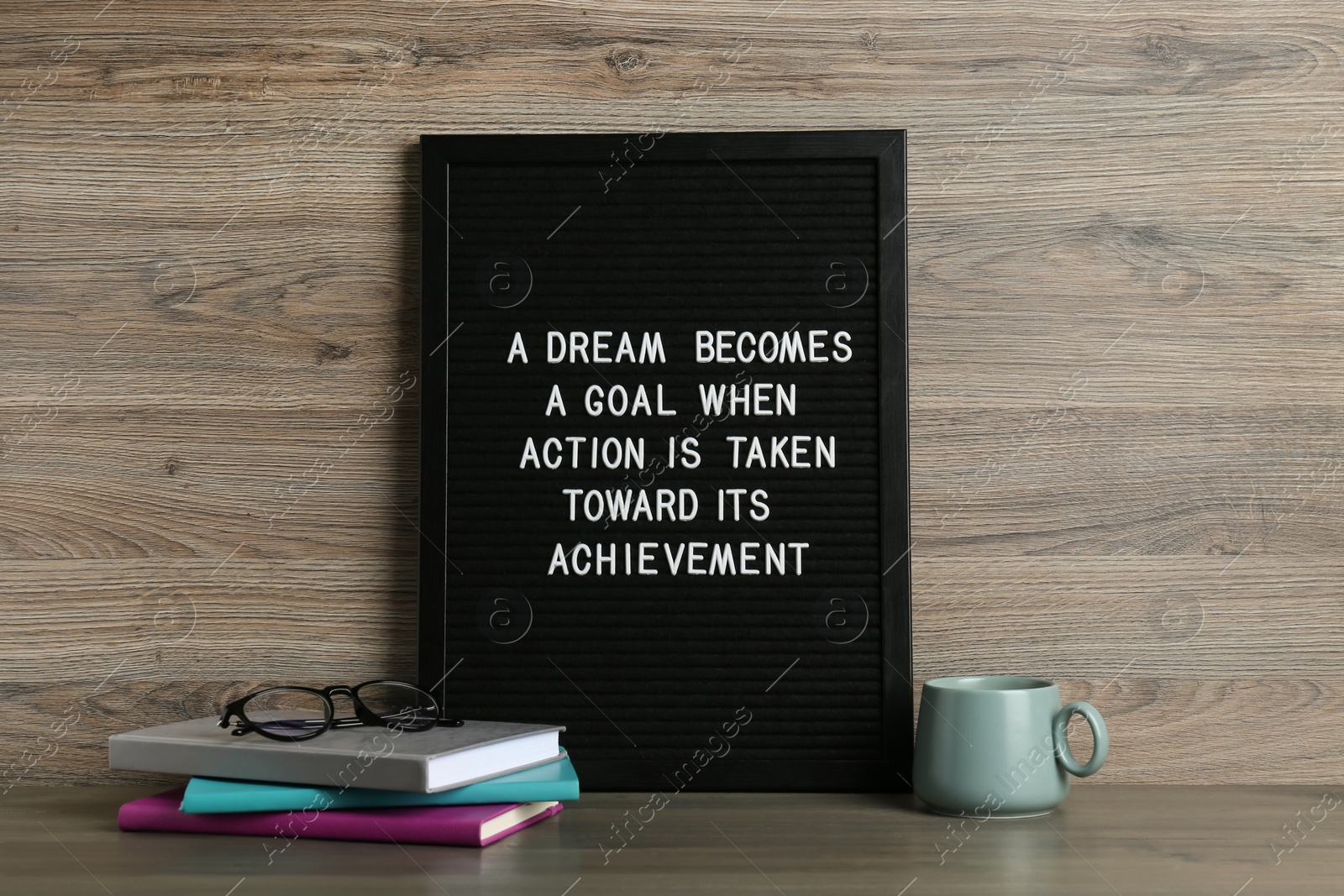 Photo of Black letter board with motivational quote a Dream Becomes a Goal When Action is Taken Toward its Achievement, notebooks and cup on wooden table