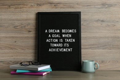 Photo of Black letter board with motivational quote a Dream Becomes a Goal When Action is Taken Toward its Achievement, notebooks and cup on wooden table