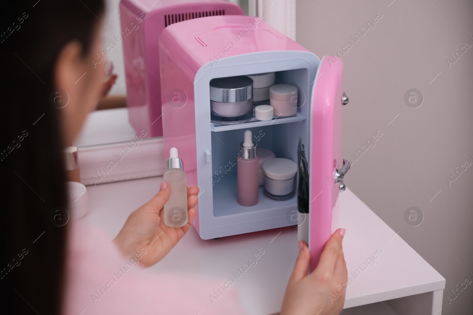 Photo of Woman taking cosmetic product out of mini refrigerator indoors, closeup