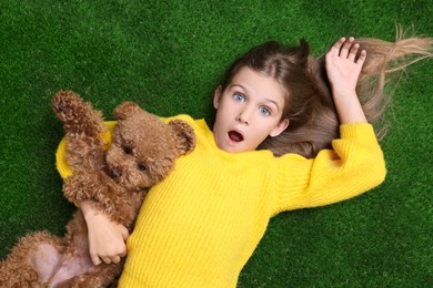 Photo of Surprised girl with cute puppy on green grass, top view. Lovely pet