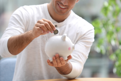 Man putting money into piggy bank against blurred background, closeup