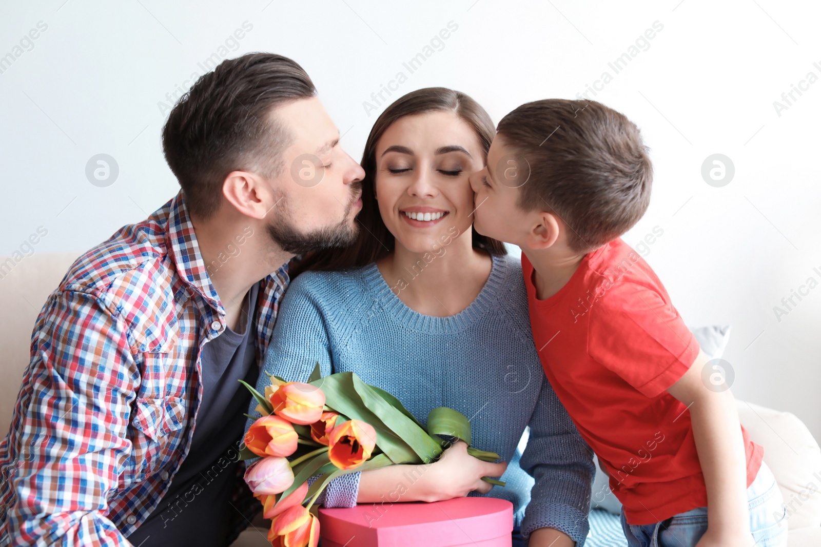 Photo of Happy woman receiving gifts from her husband and son at home. Mother's day celebration