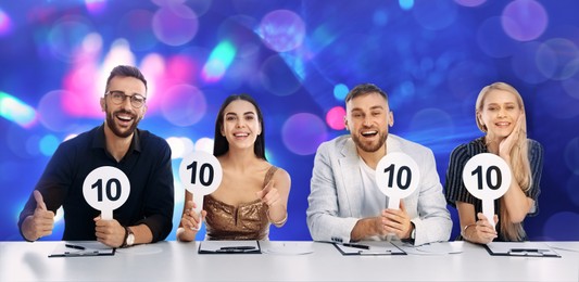 Panel of judges holding signs with highest score at table against blurred background. Bokeh effect