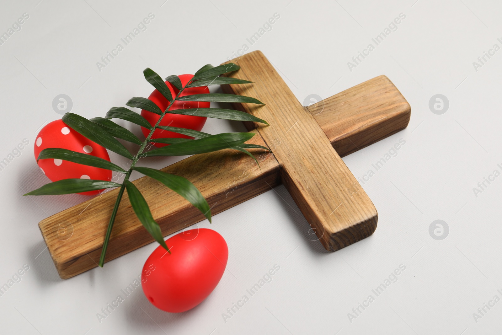 Photo of Wooden cross, painted Easter eggs and palm leaf on light grey background