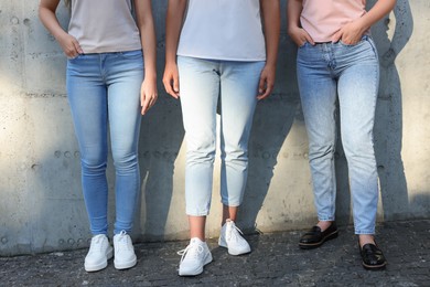 Photo of Women in stylish jeans near grey wall outdoors on sunny day, closeup