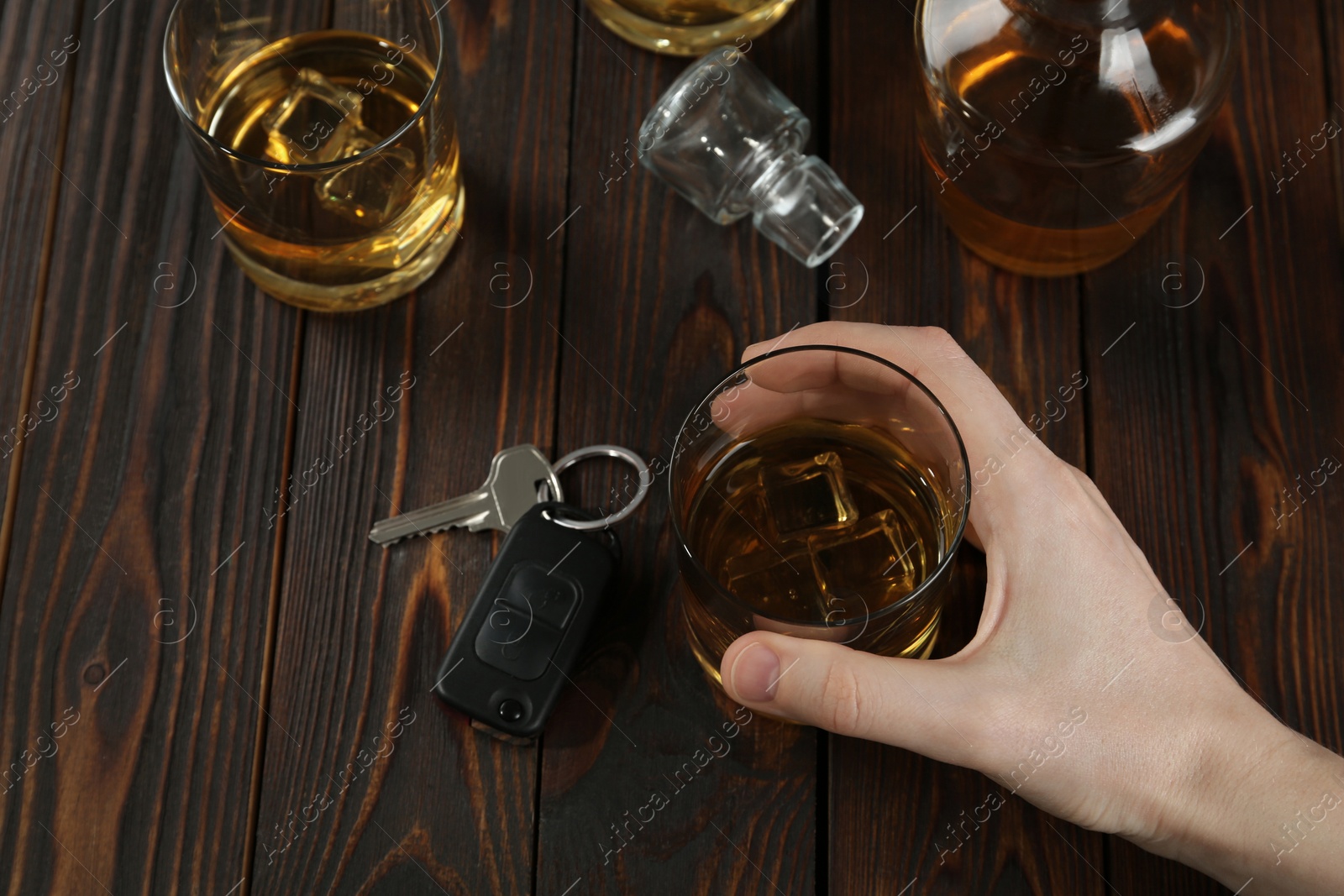 Photo of Man holding glass of alcohol near car key at wooden table, above view. Dangerous drinking and driving