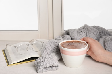 Woman holding cup of hot chocolate at window, closeup with space for text. Winter drink