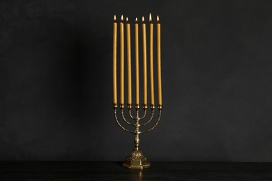 Photo of Golden menorah with burning candles on table against black background