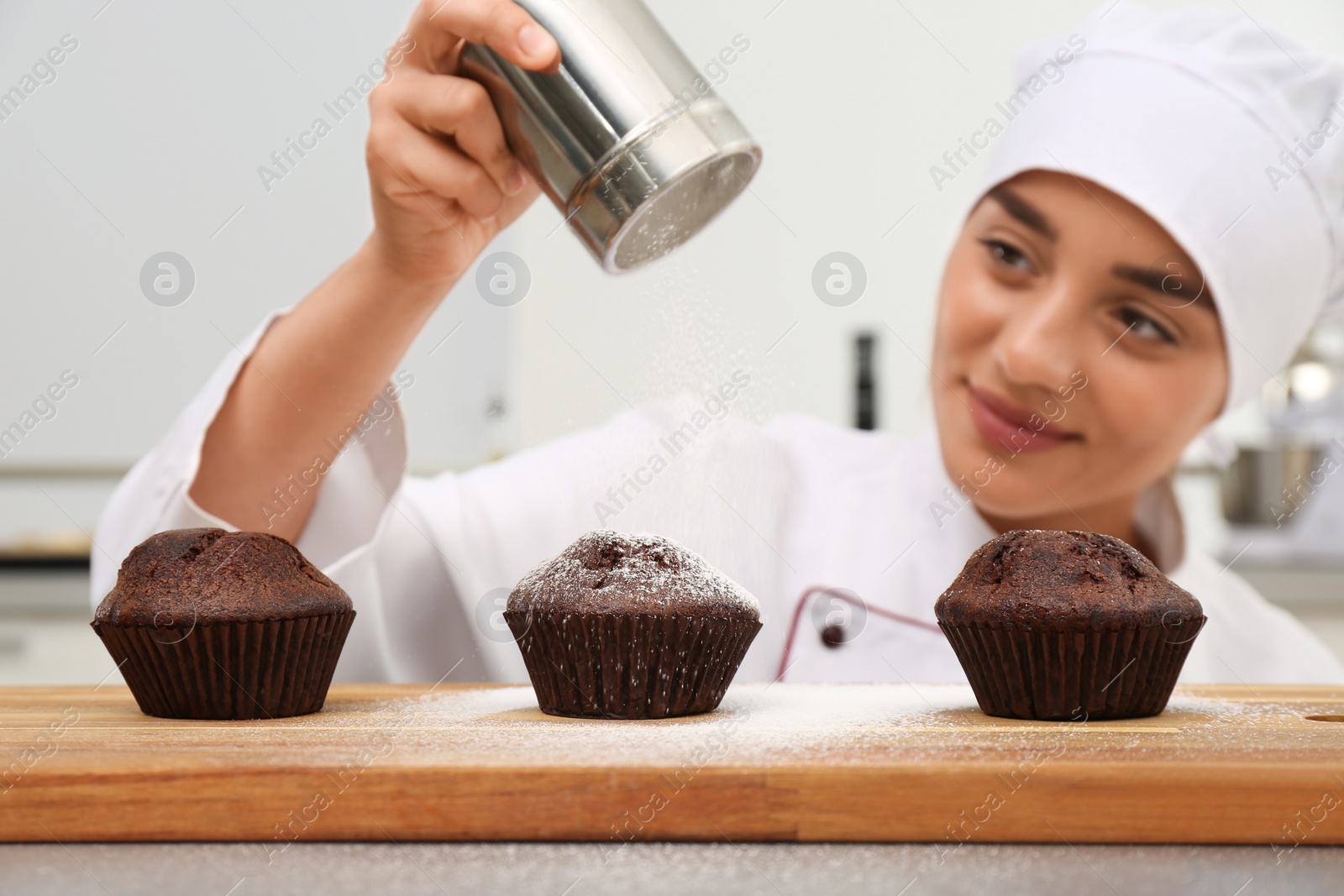 Photo of Female pastry chef sprinkling cupcakes with sugar powder in kitchen