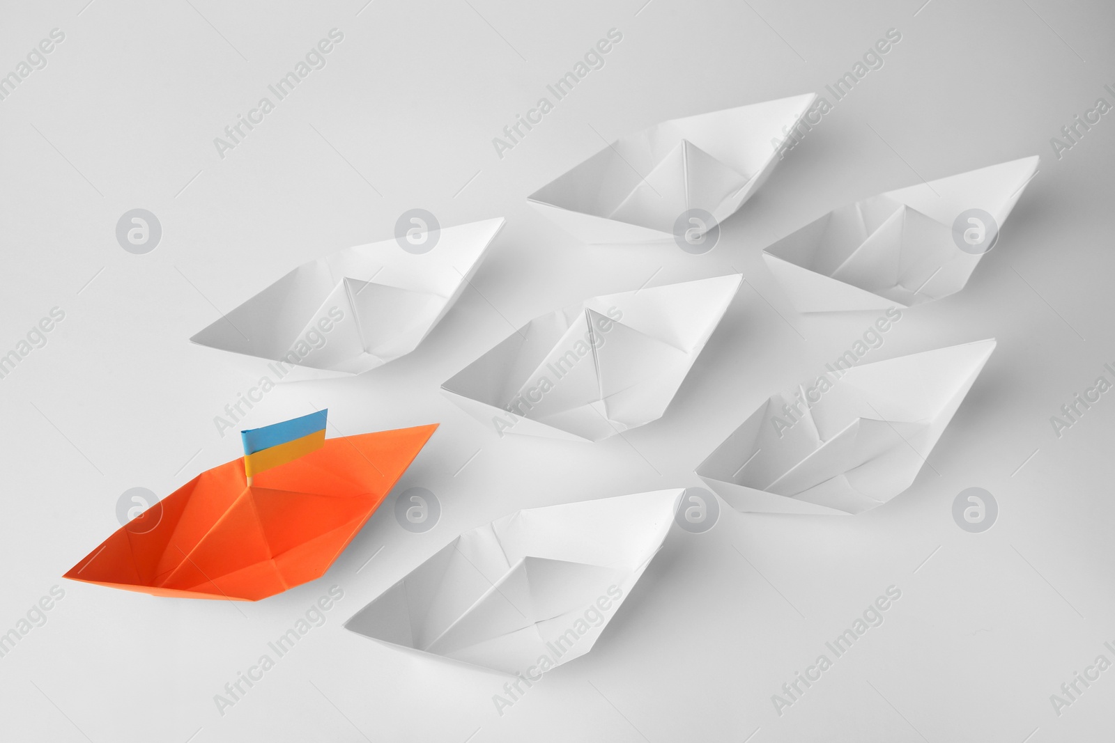 Photo of Group of paper boats following orange one on white background. Leadership concept