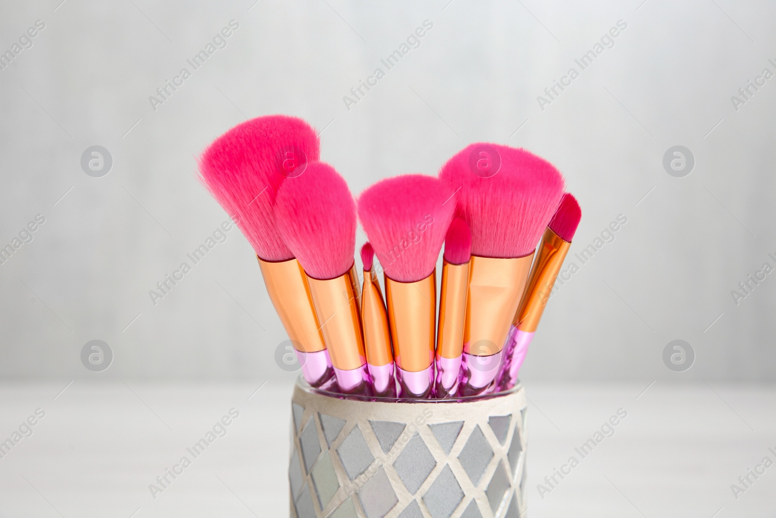 Photo of Organizer with professional makeup brushes against light background