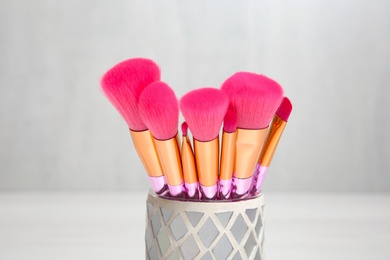 Photo of Organizer with professional makeup brushes against light background