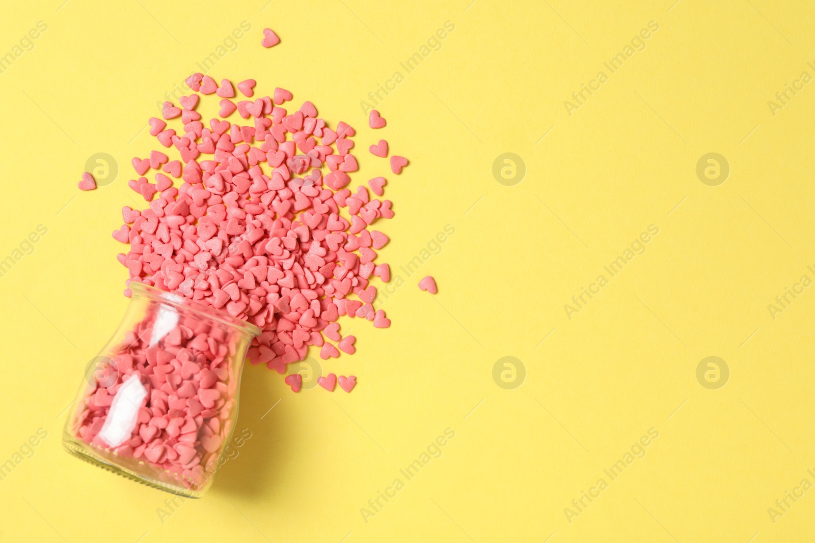 Photo of Bright heart shaped sprinkles and glass jar on yellow background, flat lay. Space for text