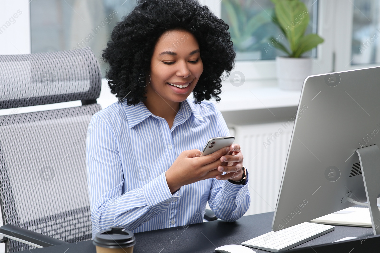 Photo of Young woman using smartphone at table in office