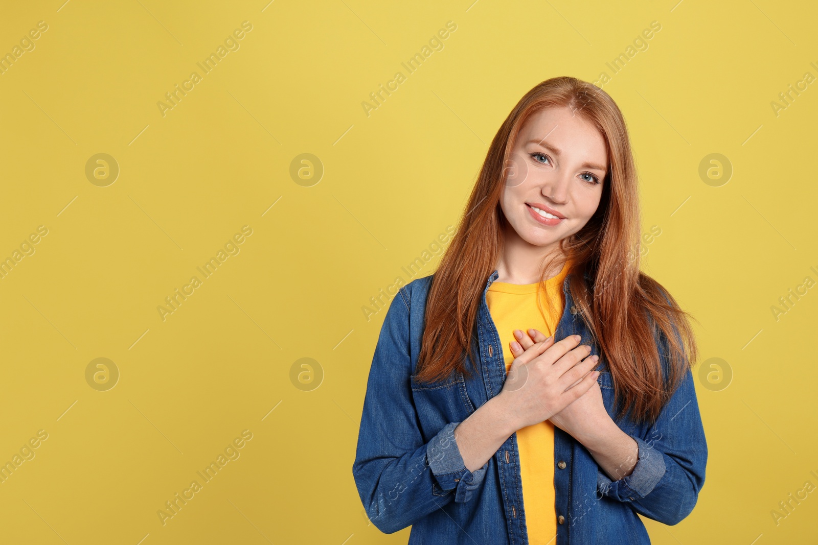 Photo of Beautiful grateful woman with hands on chest against yellow background. Space for text